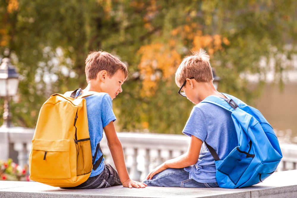 Two kids after school, sitting on bench and talking