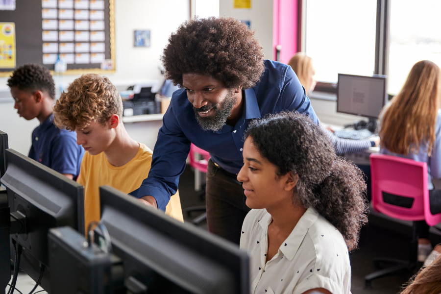 Teacher helps young girl student on the computer