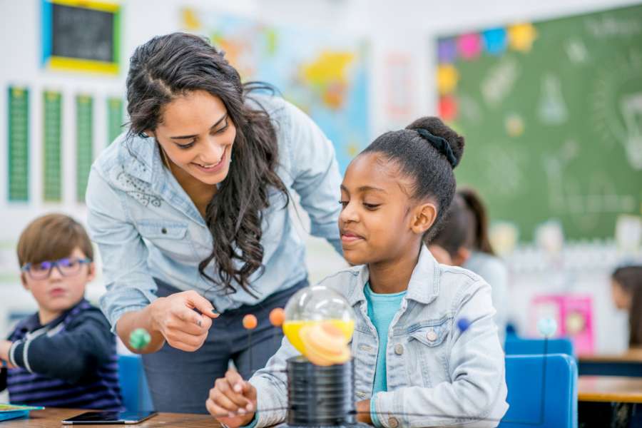 Teacher leans over students desk to help her