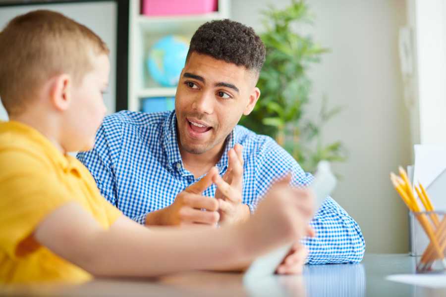 Teacher sits with student and helps him with assignment