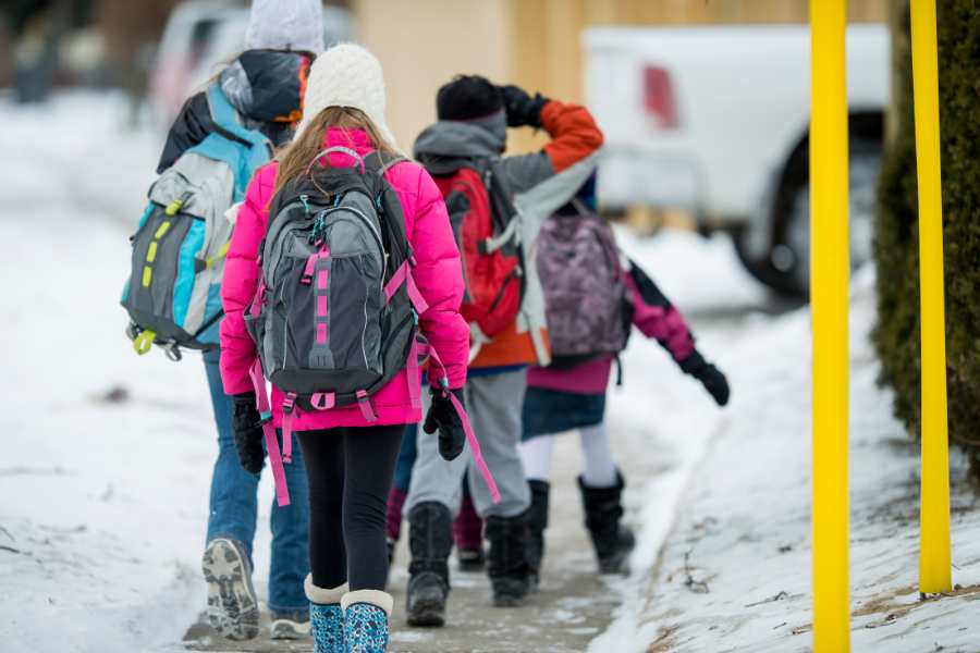 Winter Break Kids wearing multi-colored coats and boots walk home from school in the winter.