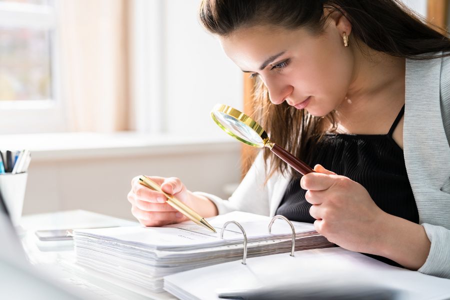 Myth vs Reality Young teacher holds magnifying glass up to curriculum book